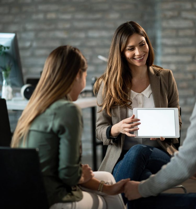 Happy insurance agent having a meeting with young couple and showing them potential investment possibilities on touchpad. Copy space.